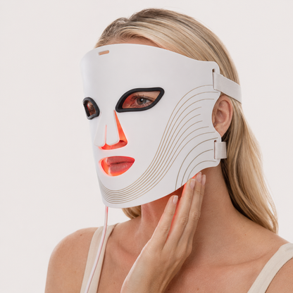 Woman wearing Morra DermaPro LED face mask glowing red, hand on her neck